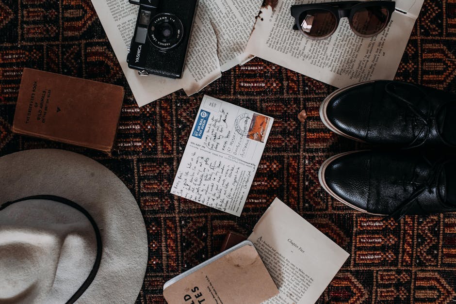 A flat lay of vintage travel items including a camera, hat, shoes, and postcards on a patterned rug.