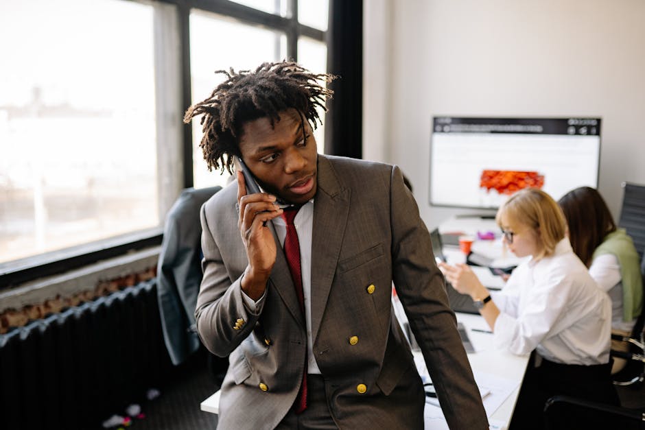 Businessman in a suit talking on the phone in a busy office environment.