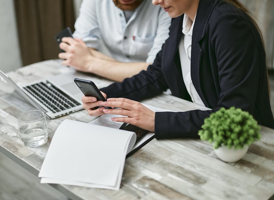 Two professionals collaborating in a business meeting using a smartphone and laptop.