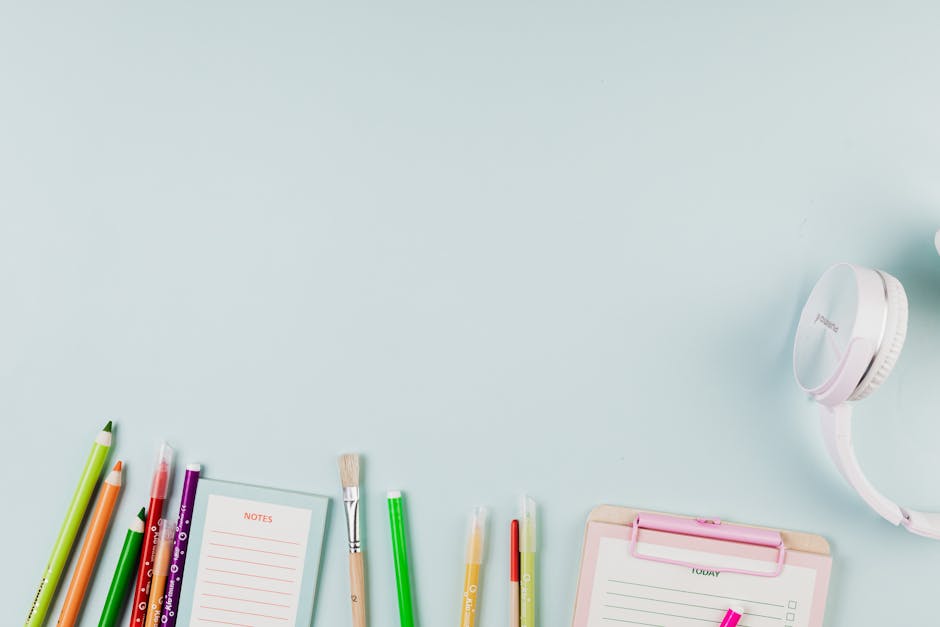 Flat lay of colorful stationery and white headphones on a blue background, ideal for creative projects.